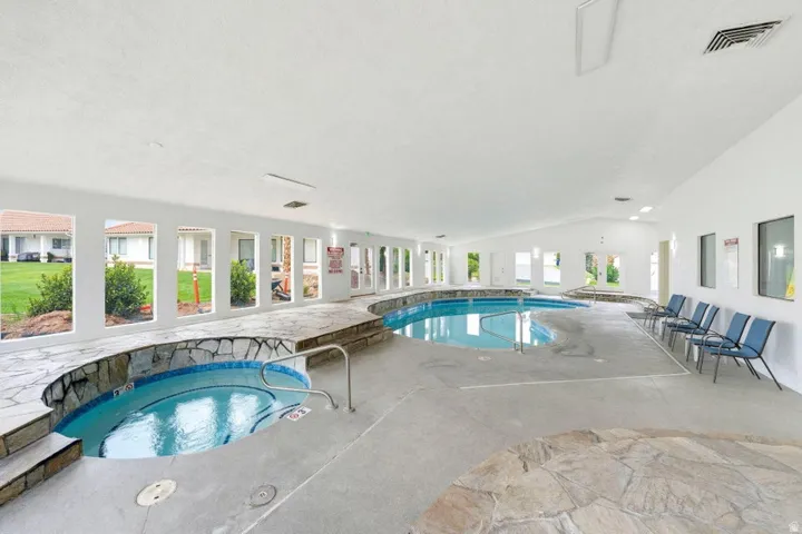 Indoor pool with a separate spa, surrounded by flagstone decking and multiple windows