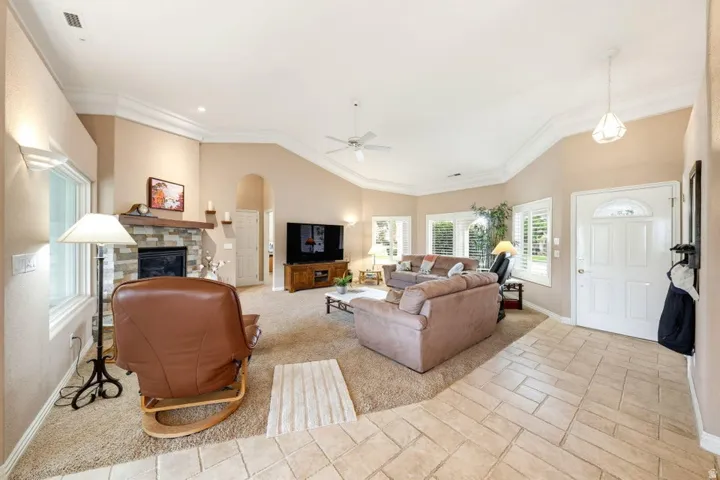 Vaulted ceilings with crown molding, stone-faced fireplace with wood mantel, arched doorway, and plantation shutters