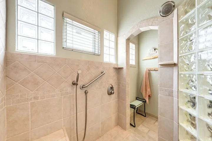 Tiled shower enclosure featuring a handheld showerhead, grab bar, and integrated bench