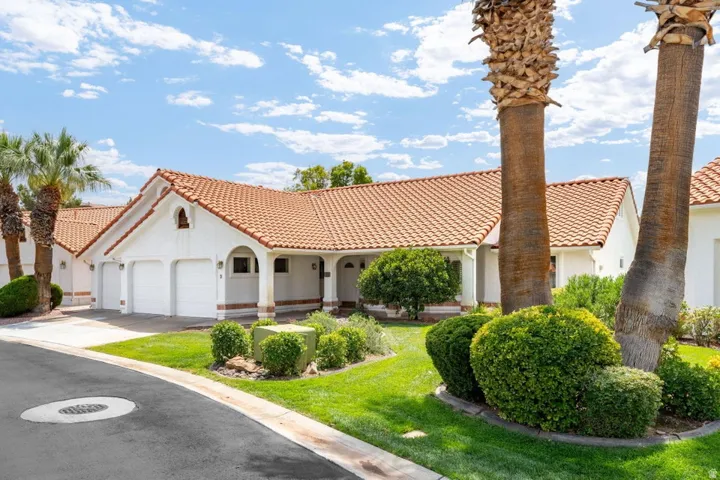 Spanish Colonial-style residence featuring a pristine white stucco exterior with clay tile roofing, multiple garage bays with arched detailing, and a circular driveway