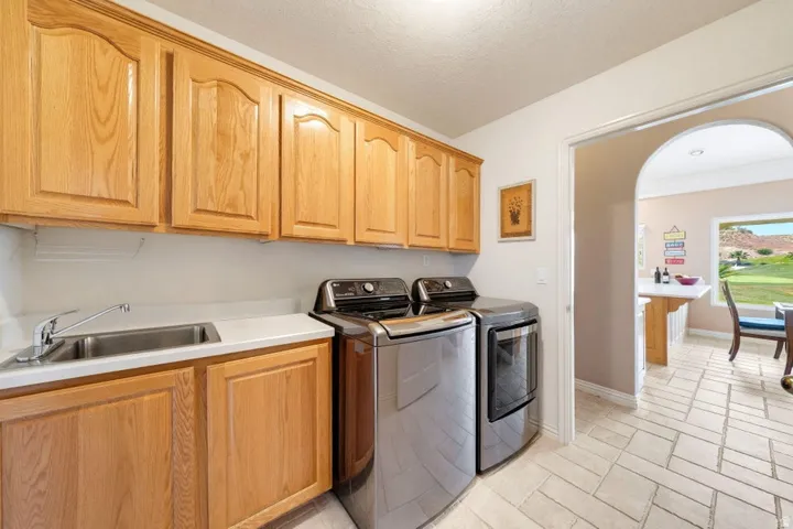 Light wood-finish cabinetry, stainless steel sink, light countertop, and light tile flooring