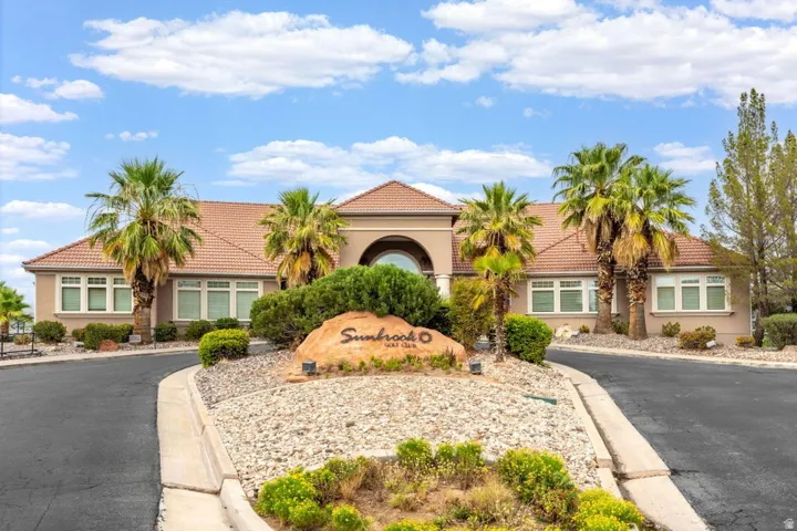 Stucco building facade with a tile roof, arched entryway, and multiple palm trees