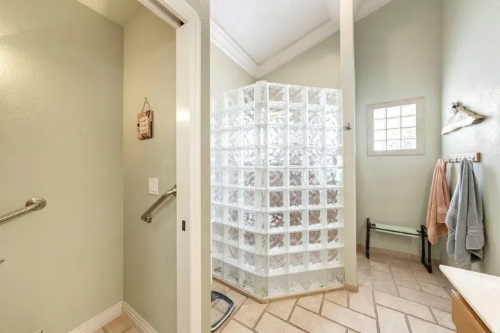Glass block shower enclosure with a transom window, vaulted ceiling, and tiled flooring