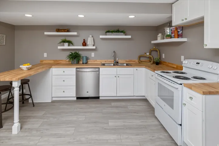 Kitchen featuring butcher block countertops, white cabinetry, stainless steel dishwasher, and wood-finish flooring