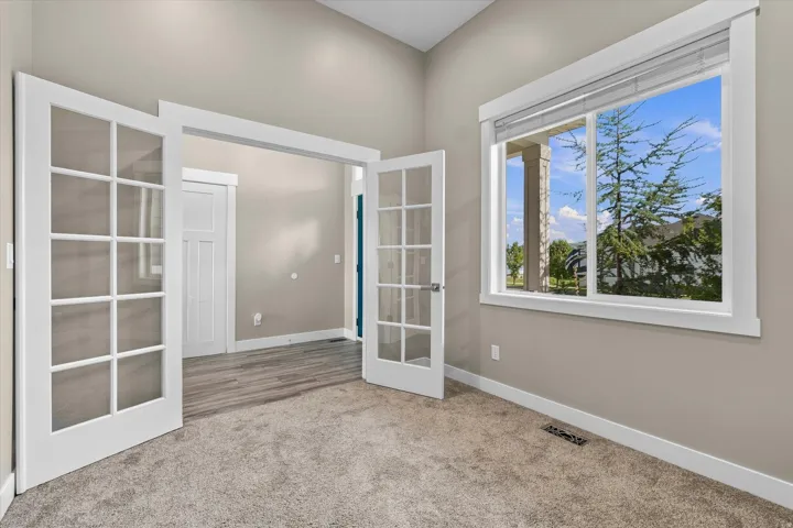 Vaulted ceiling, large window with white trim, French doors, neutral carpet, and light-colored walls