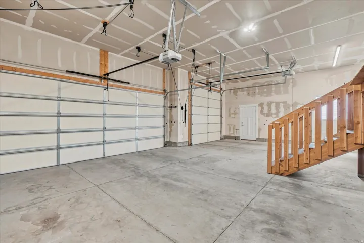 Two overhead garage doors, concrete flooring, and an unfinished wood staircase
