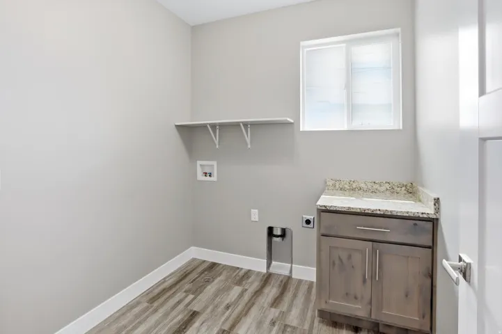 Laundry area featuring a window, wood-finish flooring, built-in shelving, and a cabinet with a stone-finish countertop