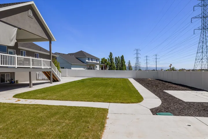 Expansive backyard featuring a covered patio, second-story deck with white railing, concrete pathways, and a privacy fence