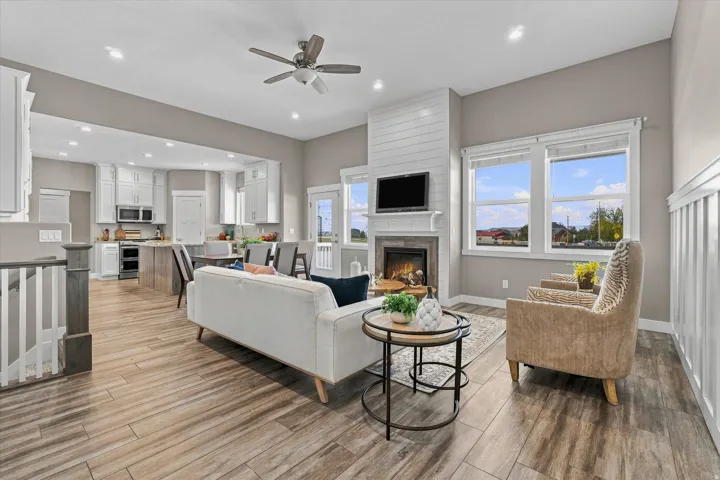 Open-concept living area featuring wood-finish flooring, a fireplace with a shiplap accent wall, white cabinetry in the kitchen, and a ceiling fan