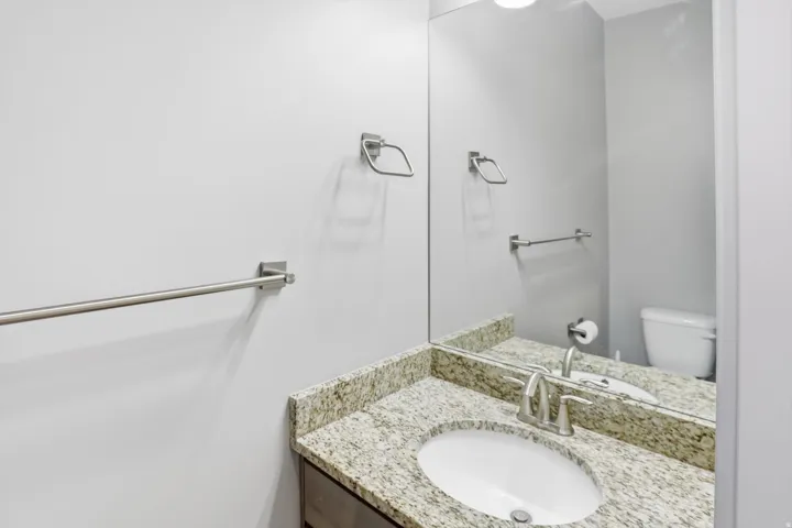 Modern bathroom featuring a granite-topped vanity with an undermount circular sink, brushed nickel hardware, and a large framed mirror