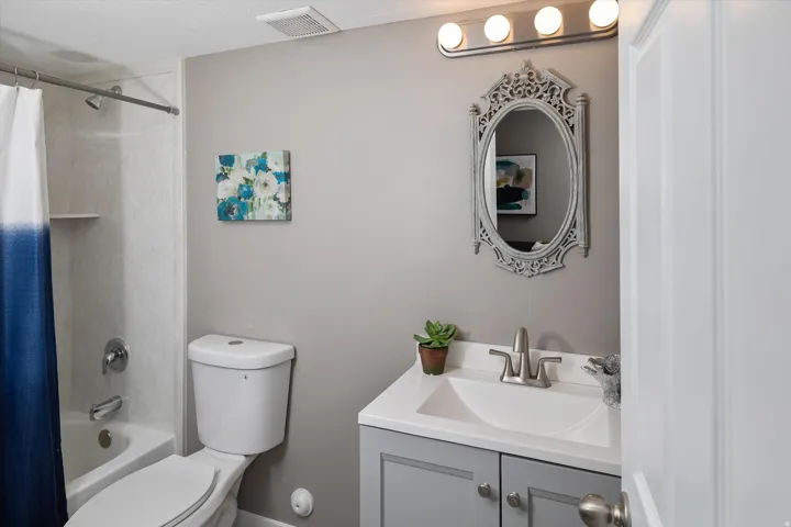 Tub and shower combination with white surround, vanity with an integrated sink, brushed nickel faucet, and decorative framed mirror