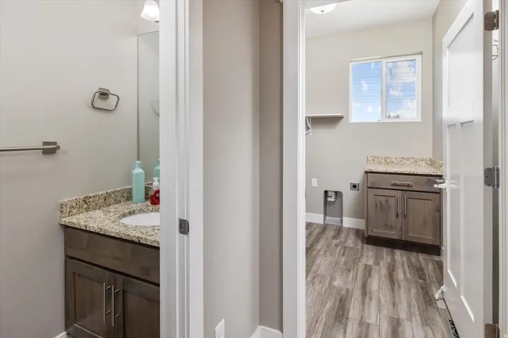 Laundry area featuring wood-finish flooring, a window, a built-in cabinet with a stone-finish countertop, and an open shelf