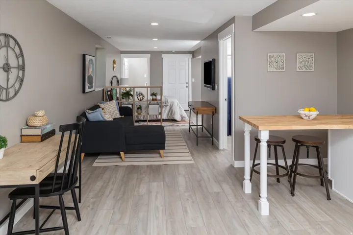 Recessed lighting, wood-finish flooring, light gray wall paint, white trim, and a built-in wood-finish breakfast bar