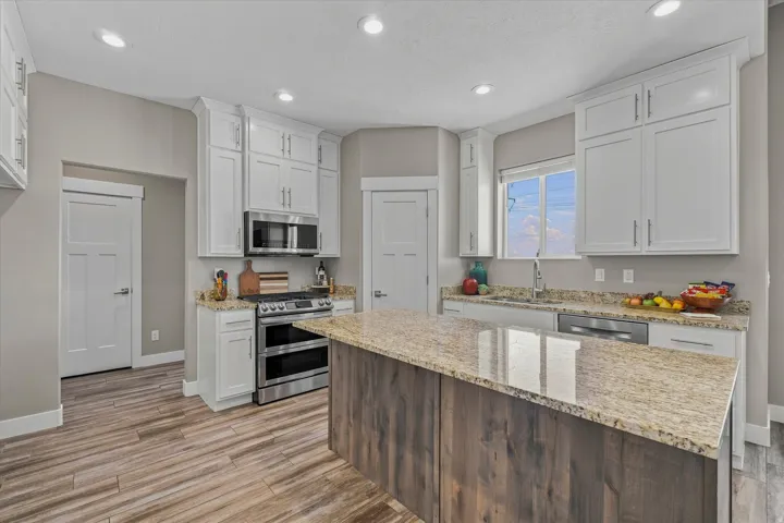 Kitchen featuring white cabinetry, stainless steel appliances, a wood-finish island with a stone countertop, recessed lighting, and wood-finish flooring