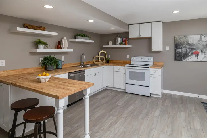 Kitchen featuring white cabinetry, butcher block countertops, stainless steel dishwasher, and wood-finish flooring