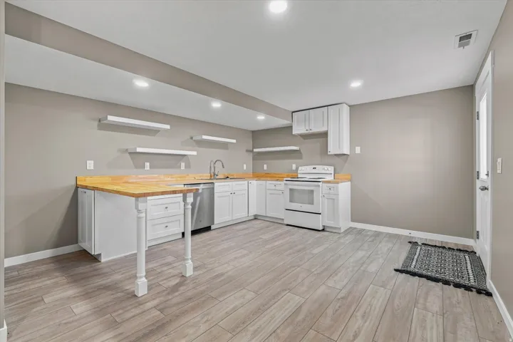 Kitchenette featuring wood-finish countertops, white cabinetry, integrated stainless steel sink, and a white oven range