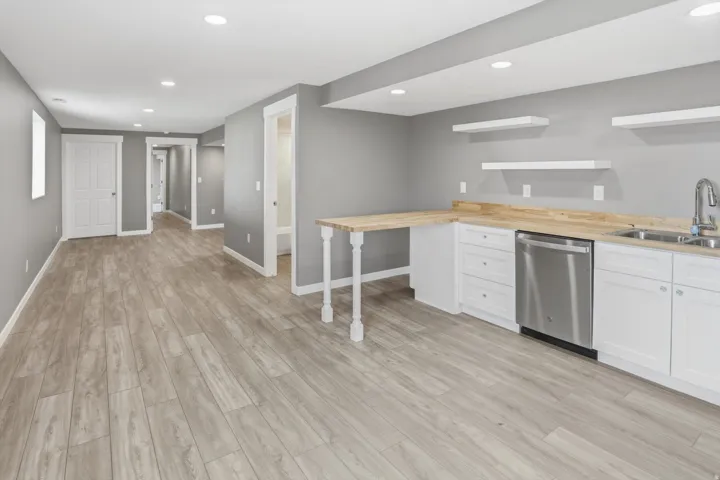 Finished basement with recessed lighting, wood-finish flooring, white cabinetry, wood countertops, and a stainless steel dishwasher