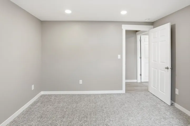Light gray walls, recessed ceiling lighting, patterned carpet flooring, white trim, and a paneled interior door