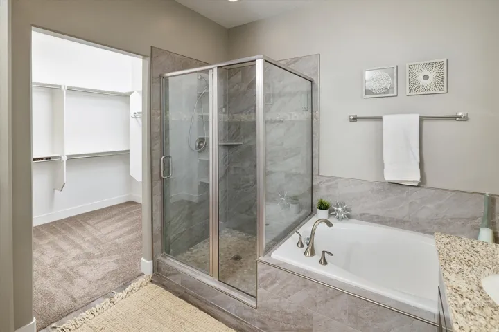 Glass-enclosed shower with a tiled surround, built-in shelf, and a soaker tub featuring a brushed nickel faucet
