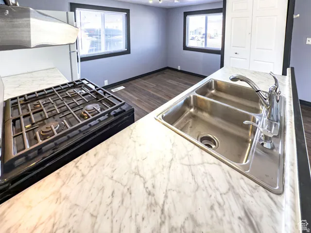 Marble-finish countertops, stainless steel double basin sink, gas range, wood-finish flooring, and white bi-fold closet doors