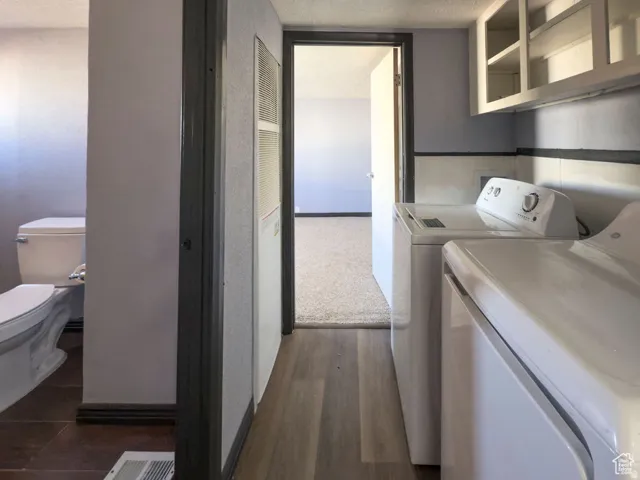 Utility area featuring a top-load washing machine, front-load dryer, wood-finish flooring, and wall-mounted cabinetry