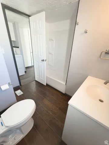 Wood-finish flooring, white vanity with integrated sink, white toilet, and a white shower/tub combination