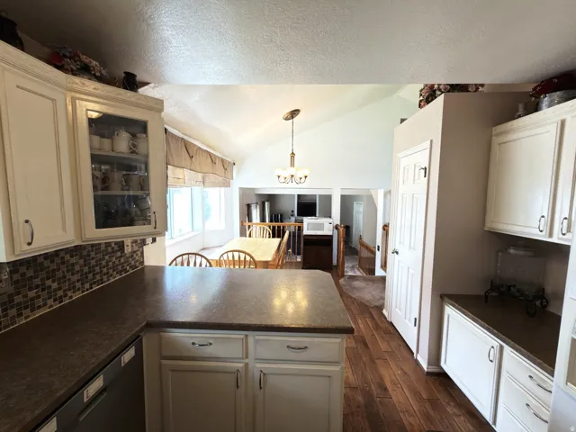 White cabinetry, mosaic tile backsplash, solid surface countertops, wood-finish flooring, and a vaulted ceiling