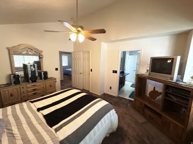 Vaulted ceiling with a ceiling fan, carpeted flooring, and a bifold door