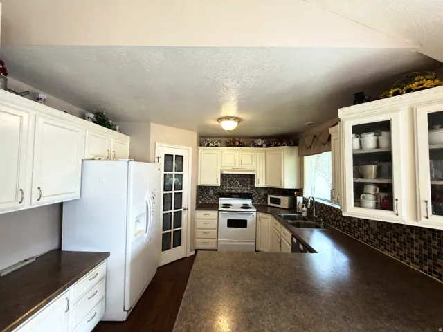 Kitchen featuring white cabinetry, a mosaic tile backsplash, a built-in double basin sink, and a multi-toned countertop