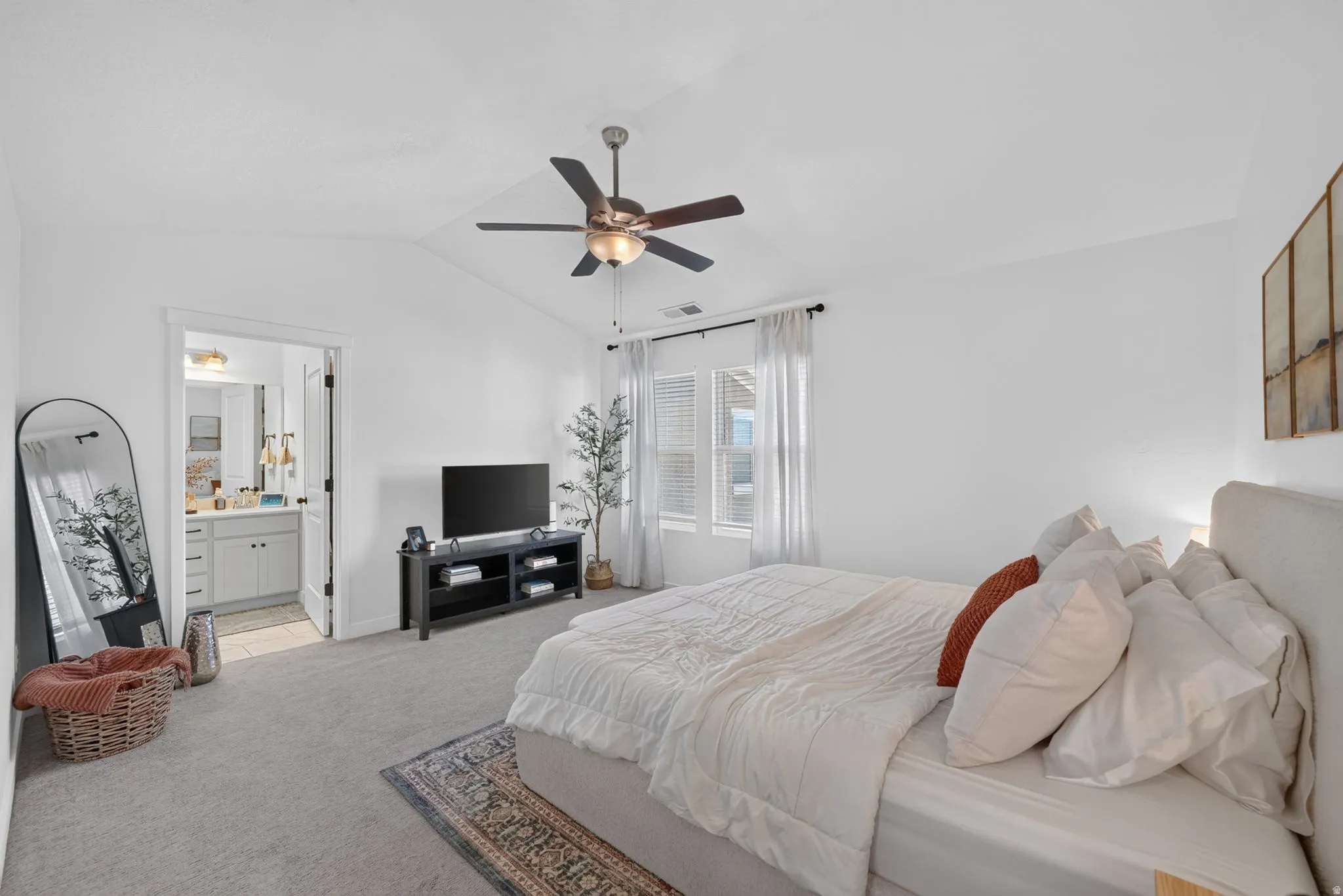 Vaulted ceiling with a ceiling fan, carpet flooring, multiple windows with blinds, and a door leading to a bathroom with a vanity
