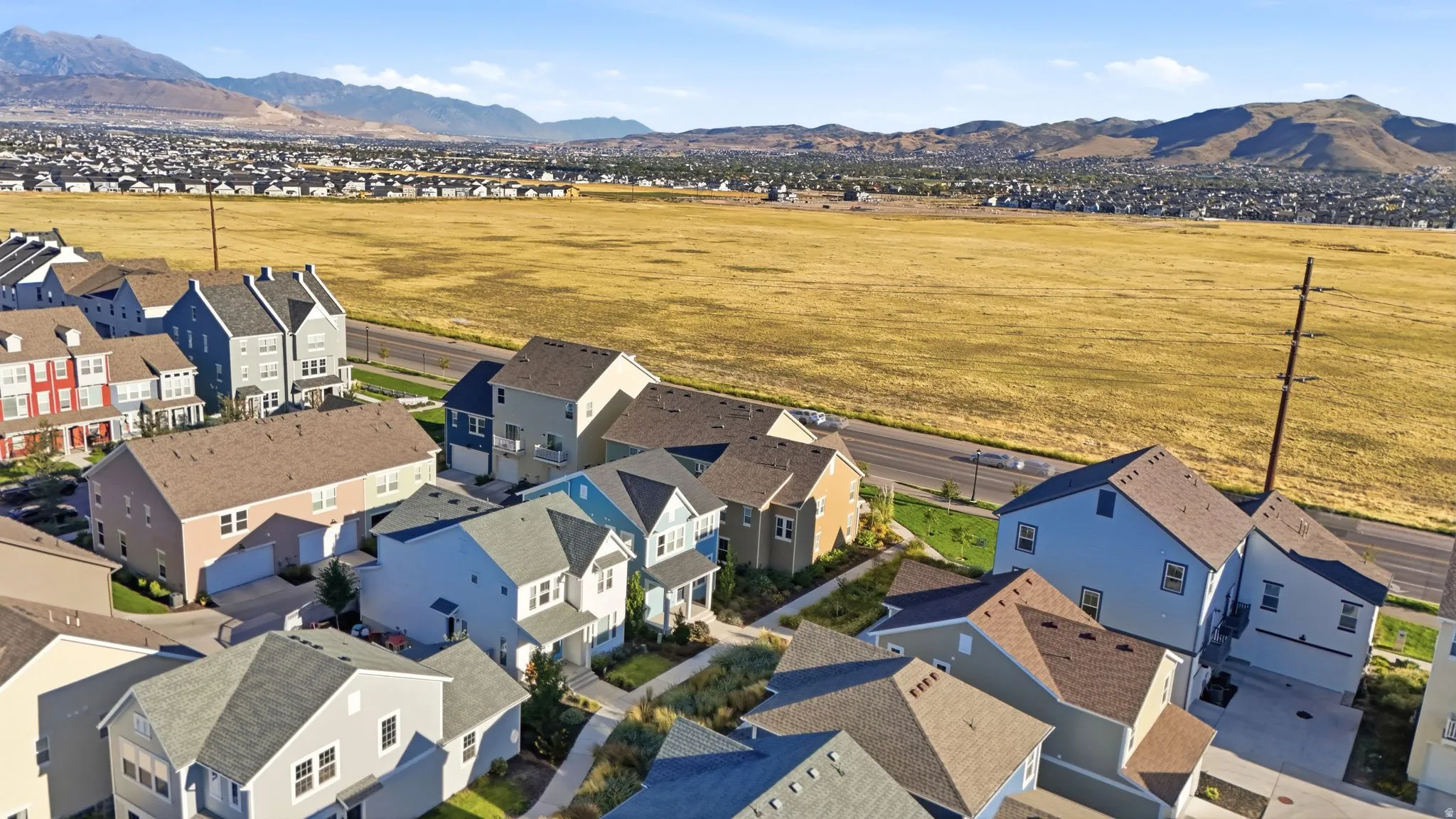 Residential neighborhood with varied architectural styles, a paved road, and distant mountain landscape