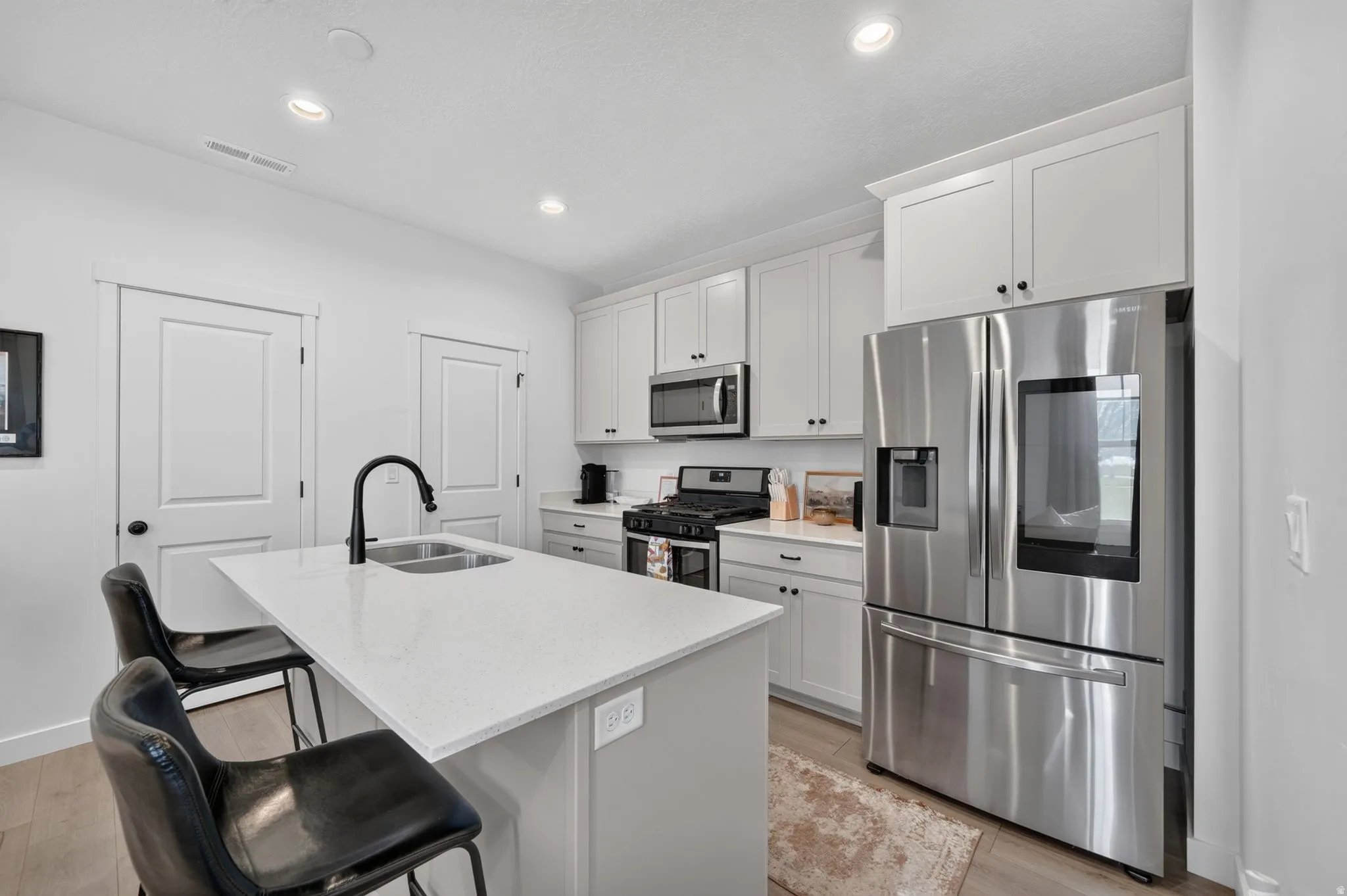 Kitchen featuring white cabinetry, stainless steel appliances, a center island with sink, black faucet, and light wood-finish flooring