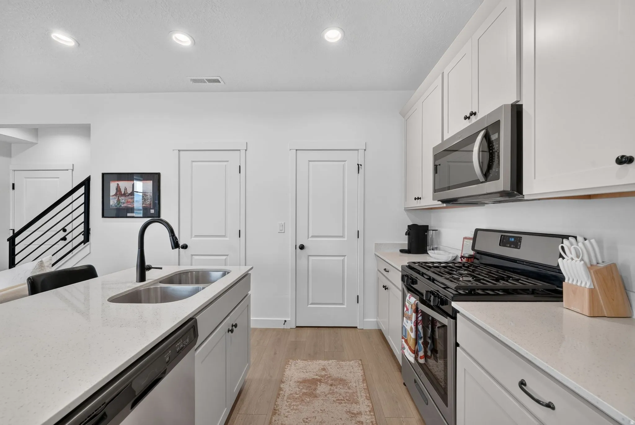 Kitchen featuring white cabinetry, light-toned countertops, stainless steel appliances, and wood-finish flooring