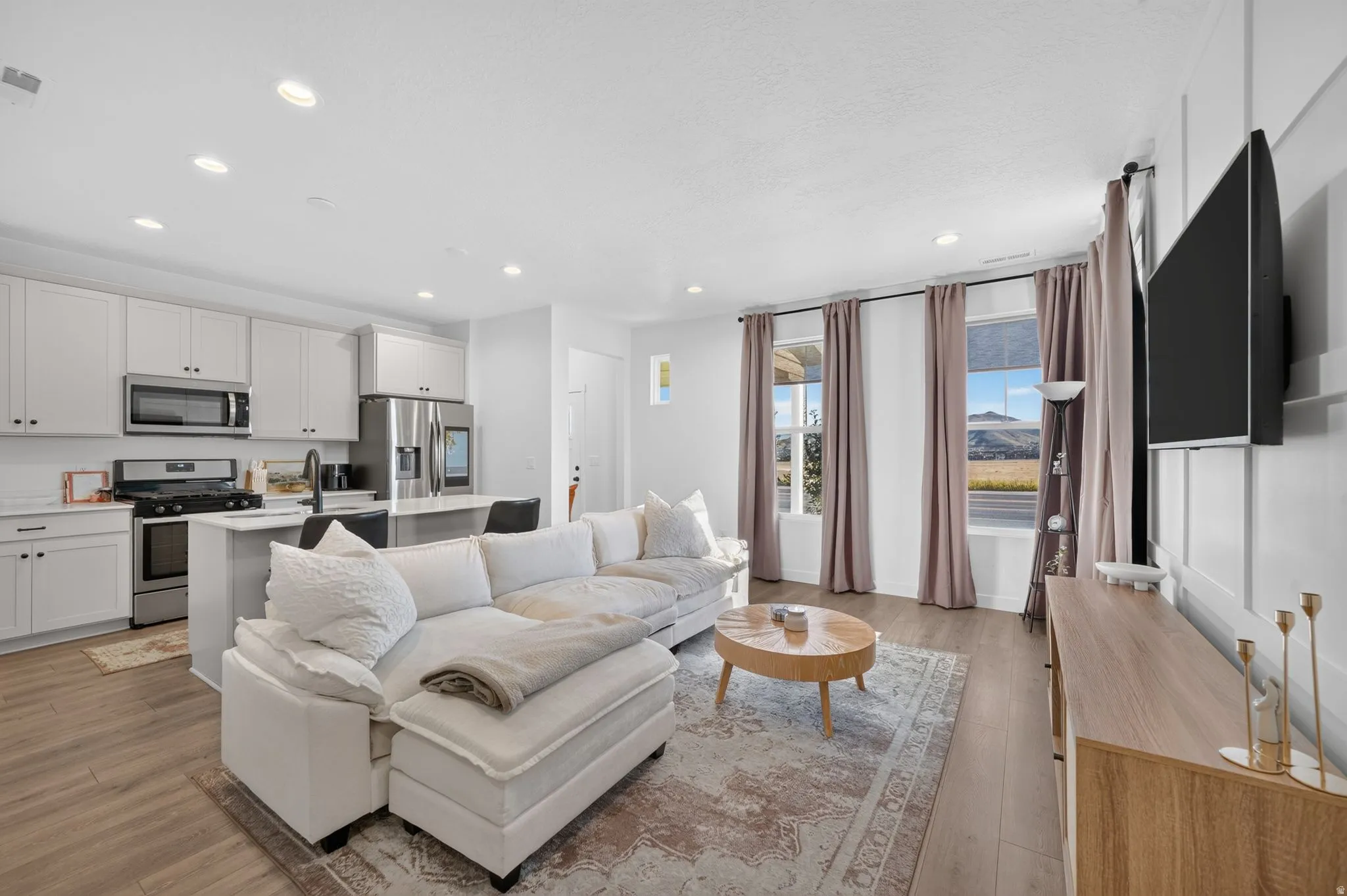 Open-concept living area with wood-finish flooring, recessed lighting, white kitchen cabinetry, stainless steel appliances, and a kitchen island with seating