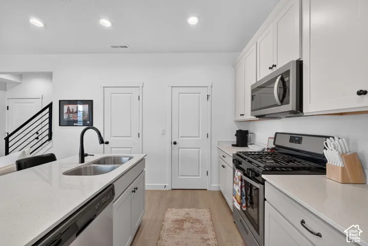 Kitchen featuring white cabinetry, light-toned countertops, stainless steel appliances, and wood-finish flooring
