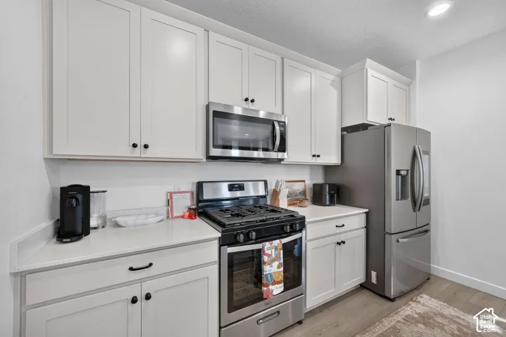 White shaker-style cabinetry, stainless steel appliances, light-toned countertops, and light wood-finish flooring