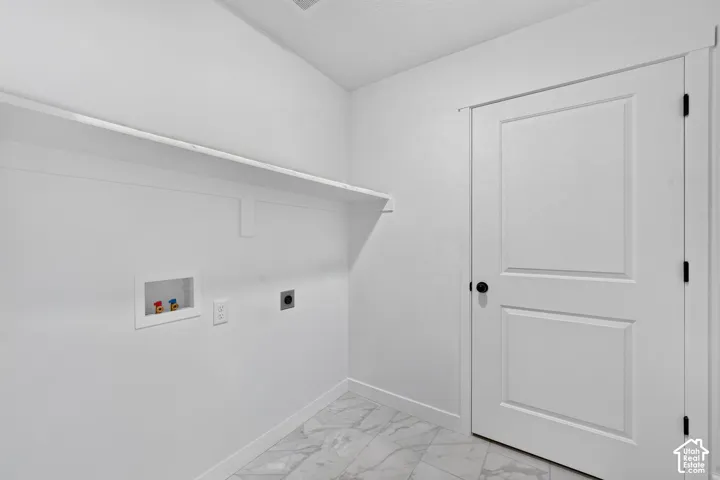 Bright laundry room featuring polished marble-finish flooring, white shaker-style cabinetry with integrated shelving, recessed electrical outlets, and a two-panel white interior door with black hardware