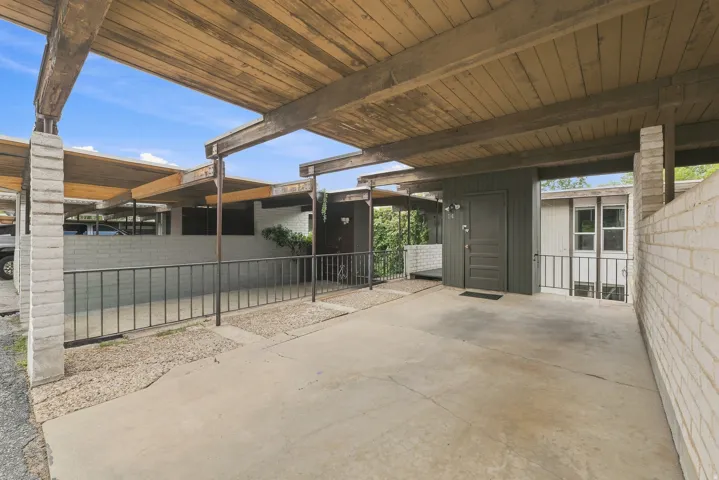 Covered carport featuring exposed wood beams and concrete flooring