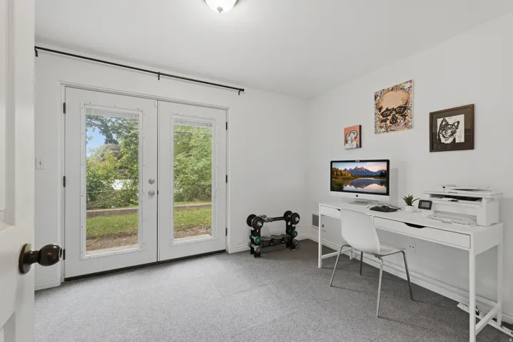 White walls, light gray carpet flooring, and double French doors with interior blinds