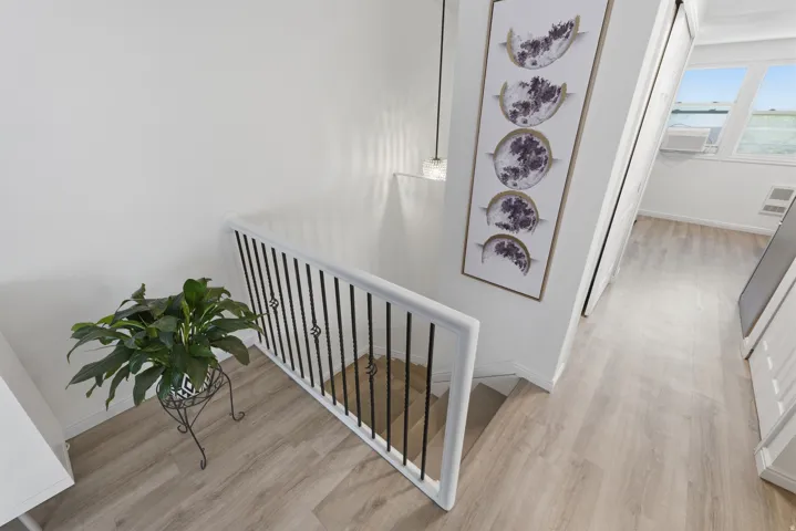 Wood-finish flooring throughout, white walls, and a staircase with a white handrail and black metal balusters