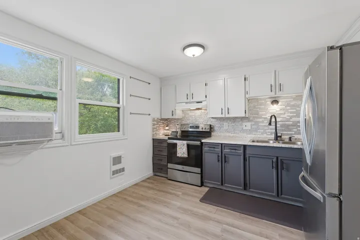 Updated kitchen featuring stainless steel appliances, wood-finish flooring, two-tone cabinetry, and a tile backsplash