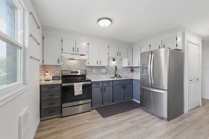 Kitchen featuring stainless steel appliances, two-tone cabinetry, mosaic tile backsplash, and light wood-finish flooring