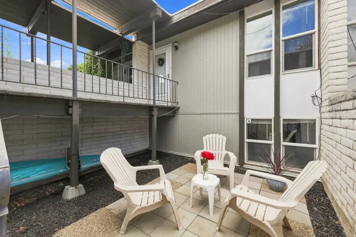 Private patio with paver flooring, overhead balcony, and brick architectural elements