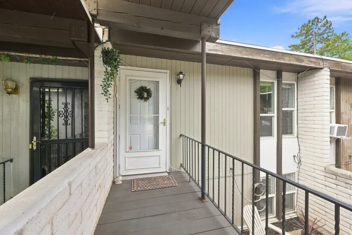 Front porch with a white paneled door, black wrought iron railing, and brick half-wall
