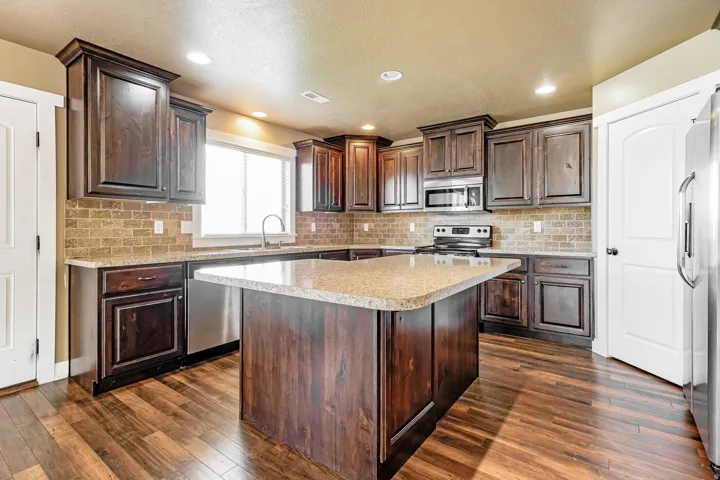 Spacious kitchen featuring dark wood cabinetry, a central island with granite-style countertops, wood-finish flooring, a tile backsplash, and stainless steel appliances