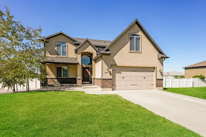 Two-story stucco exterior with brick accents, arched entry with transom window, attached garage, and a concrete driveway