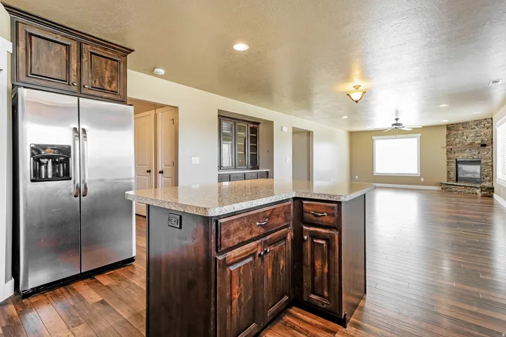Spacious open-concept living area featuring wood-finish flooring, a stone-faced fireplace, and a kitchen island with a light-toned countertop