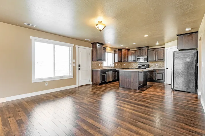 Wood-finish flooring throughout, dark wood kitchen cabinetry, kitchen island with counter seating, stainless steel appliances, and a tile backsplash