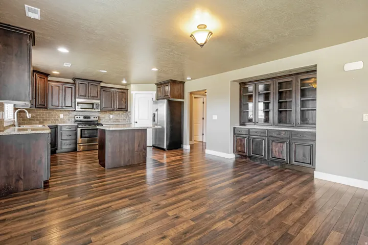 Open-concept space featuring wood-finish flooring, dark wood cabinetry, a central kitchen island, stainless steel appliances, and a built-in display cabinet with glass fronts