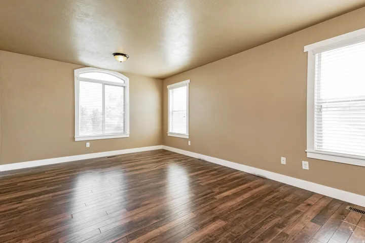 Wood-finish flooring, neutral wall color, arched window, additional rectangular windows, and a flush mount ceiling light